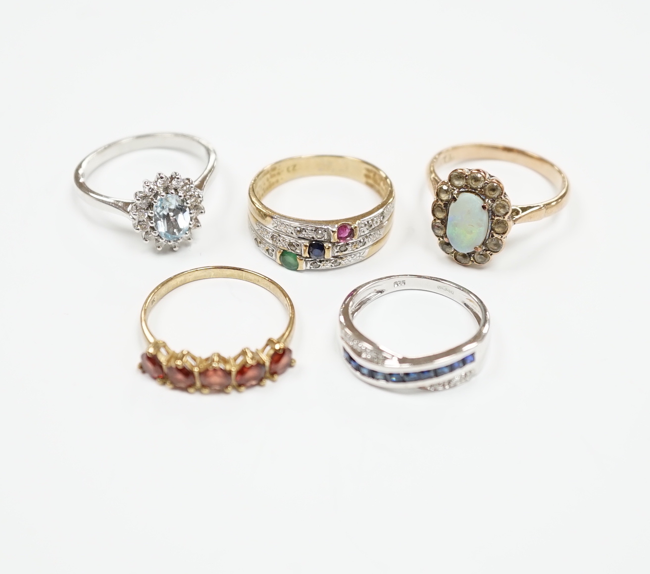 Four assorted 9ct and gem set rings, including opal and white sapphire?, blue topaz and diamond, sapphire and diamond chip crossover and five stone garnet? and a yellow metal and four colour cubic zirconia ring, gross we